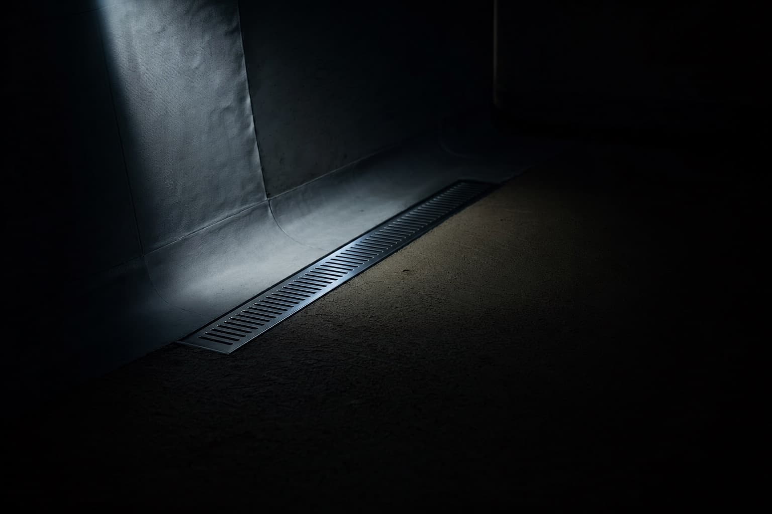 A shower floor under construction, its waterproofing membrane folded up the wall and a linear drain set flush